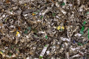 Pile of shredded electronic waste showing fragments of metal, green circuit boards, and plastic from recycled devices